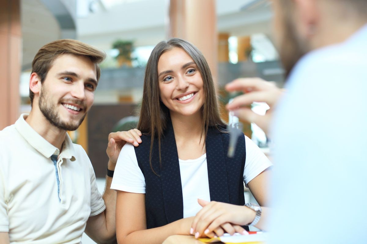 Close up of real estate agent giving keys to couple of customers.